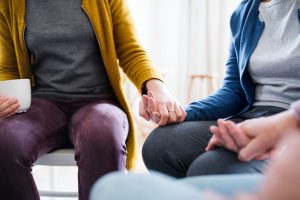 Midsection of men and women sitting in a circle during group therapy, supporting each other and holding hands.